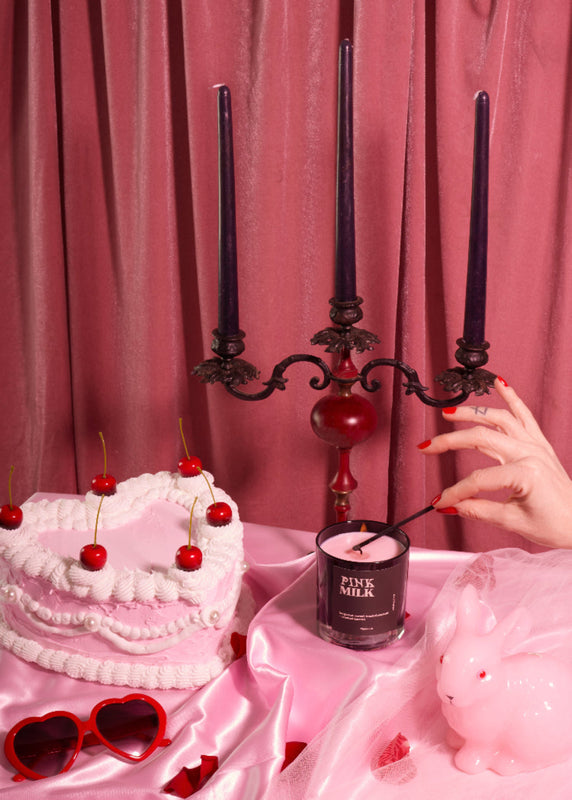 Nightwork Candle “Pink Milk” luxury soy candle styled in a whimsical still life with heart-shaped cake, cherries, pink satin, black taper candles, and vintage décor, evoking sweet indulgence, gothic romance, and nostalgic dessert fantasy.